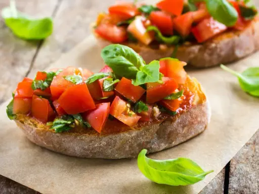 Zwei Bruschetta mit frischen Tomaten und Basilikum, warm oder kalt serviert, auf rustikalem Holztisch.