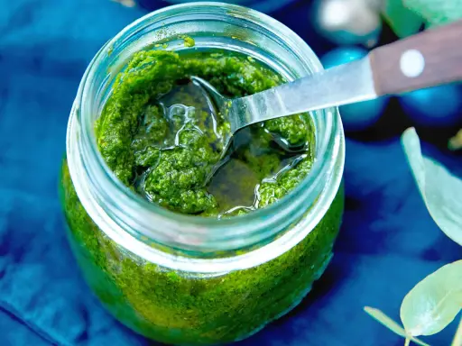 Frisches Rucola Pesto in einem Glas, bereit zum Genießen. Eine Löffelspitze ragt heraus.