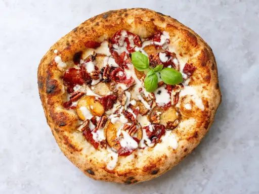 Pizza mit karamellisierten Zwiebeln, Speck, Pekannüssen und einem Hauch von Parmesan. Ein grünes Basilikumblatt krönt das Kunstwerk.