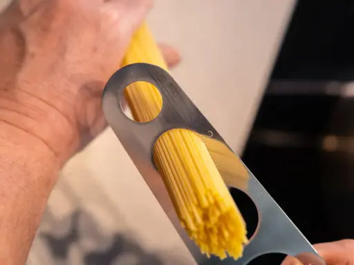 Ein Mann misst mit einem Metallwerkzeug die richtige Menge Spaghetti pro Person ab.