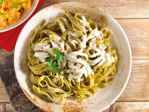 Grüne Bandnudeln mit cremiger Gorgonzola-Sauce, garniert mit Petersilie und roten Pfefferflocken.