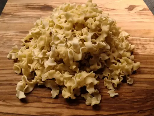 Ein Haufen ungekochte Pasta aus Hartweizengrieß (semola) liegt auf einem Holzbrett.