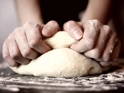 Hände kneten Teig, um die perfekte Konsistenz für Pizza zu erreichen. Die Frage "wie lange pizzateig kneten" beschäftigt viele Hobbybäcker.