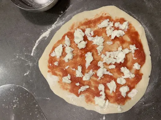 Ein roher Pizzaboden mit Tomatensauce und Mozzarella. Der pizzateig zieht sich zusammen, bereit für den Ofen.