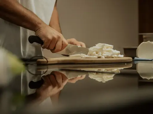 Hände schneiden Fior di Latte auf einem Holzbrett. Die frische Mozzarella-Masse wird für das Einfrieren vorbereitet.