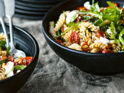 Zwei Schalen mit einem köstlichen nudelsalat mit getrockneten tomaten, Pinienkernen und Rucola.