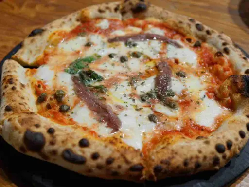 Eine original Pizza mit geschmolzenem Käse, Sardellen, Kapern und Basilikum.