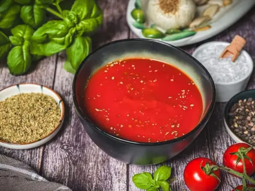 Schüssel mit original italienischer pizzasauce, umgeben von frischem Basilikum, Tomaten, Knoblauch, Salz und Pfeffer.