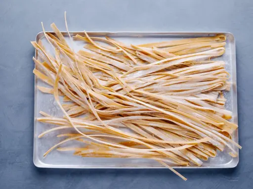 Frische, selbstgemachte Tagliatelle liegen auf einem Blech, bereit zum Kochen. Das Ergebnis von Tagliatelle selber machen.