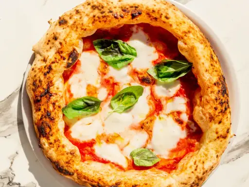 Eine klassische Pizza Napoli mit Tomaten, Mozzarella und frischem Basilikum. Der Belag ist einfach, aber perfekt für diese neapolitanische Spezialität.