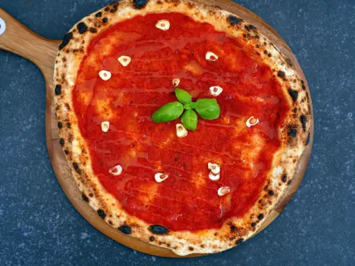 Eine köstliche Pizza Marinara mit Tomatensauce, Knoblauchscheiben und frischem Basilikum auf einem Holzbrett.