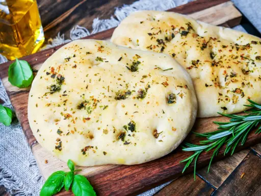 Zwei fluffige Pizzabrote mit Kräutern, perfekt gebacken mit Trockenhefe. Daneben frisches Basilikum und Rosmarin.