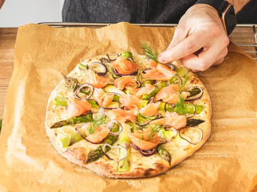 Eine köstliche Pizza mit Lachs, Spargel und roten Zwiebeln wird mit frischem Dill garniert.
