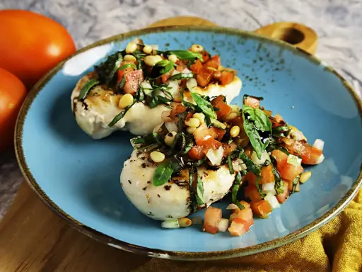 Zwei Hähnchenbrustfilets mit frischer Tomaten-Basilikum-Mischung und Pinienkernen, beträufelt mit Balsamico. Köstliche Bruschetta-Variante.