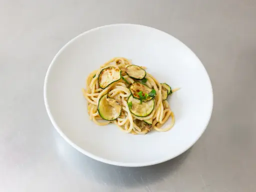 Spaghetti alla Nerano, ein cremiges Pastagericht mit gebratenen Zucchinischeiben, garniert mit frischen Kräutern, serviert auf einem weißen Teller.