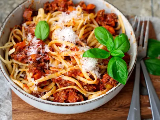 Eine Schüssel mit Linguine und einer herzhaften, **schnellen Bolognese**. Garniert mit frischem Basilikum und Parmesan.