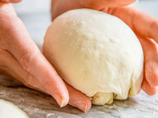 Hände formen einen Teigball, bereit zum stretch and fold pizza.
