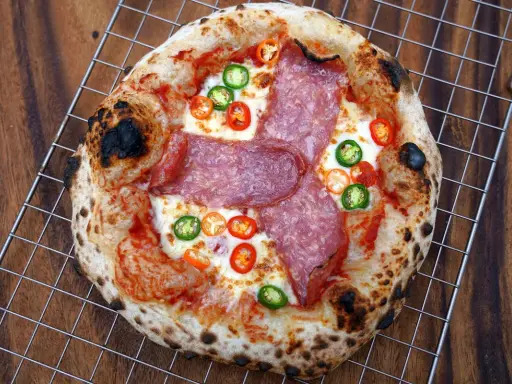 Eine scharfe Salami Pizza mit geschmolzenem Käse und bunten Chilischeiben auf einem Gitterrost.