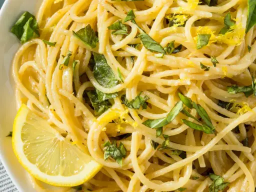 Spaghetti al limone, garniert mit frischem Basilikum und Zitronenschale, serviert mit einer Zitronenspalte.