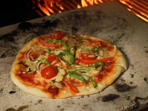 Eine köstliche Pizza mit Tomaten, Paprika und Pilzen wird auf einem Pizzastein im Ofen gebacken, wo die Flammen lodern.