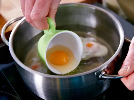 Ein rohes Ei wird aus einer grünen Tasse in kochendes Wasser gegossen, um Eier zu pochieren.