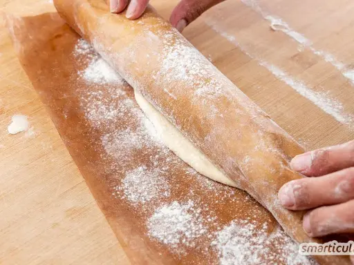 Hände rollen Teig auf Backpapier aus. Perfekt, um gegangenen Pizzateig einzufrieren und später zu verwenden.