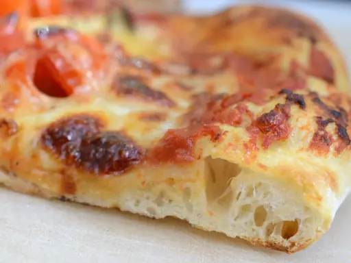 Ein Stück Pizza mit luftigem pizzateig, frisch aus dem pizzaofen. Der Teig ist goldbraun gebacken, die Tomatensoße und der Käse sind perfekt geschmolzen.