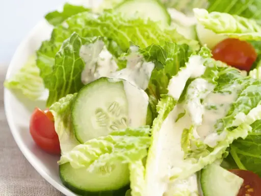 Frischer Romana Salat mit Gurkenscheiben und Tomaten, beträufelt mit cremigem Dressing.