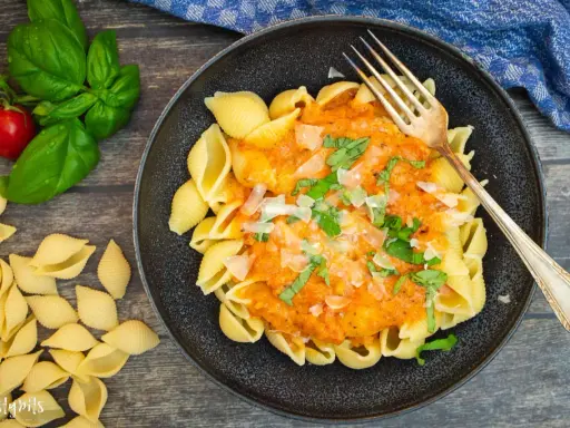Herzhafte Muschelnudeln mit cremiger Tomaten-Sahne-Sauce, garniert mit frischem Basilikum und Parmesan. Ein Genuss!