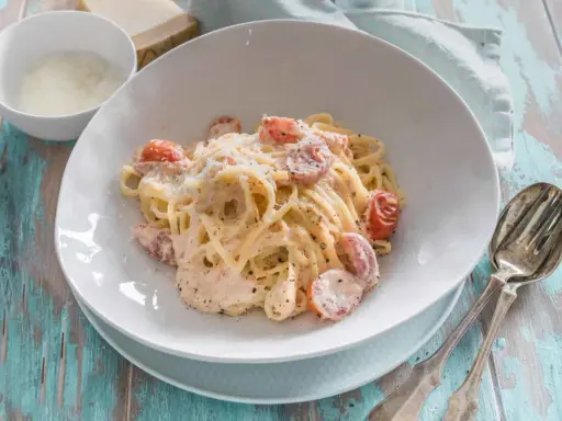 Cremige Pasta al Salmone mit Kirschtomaten und Parmesan, serviert auf einem rustikalen Holztisch.