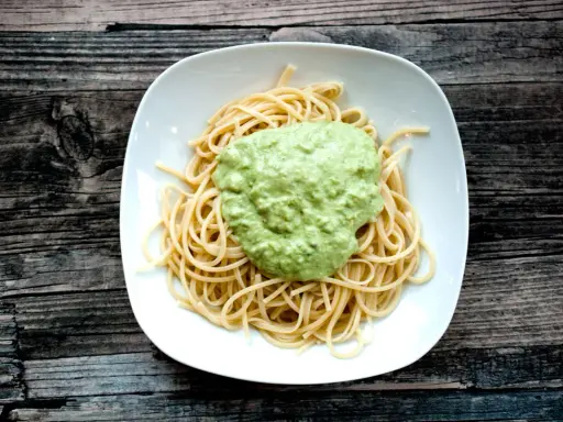 Spaghetti mit cremigem Avocado Pesto auf einem weißen Teller, serviert auf rustikalem Holz.