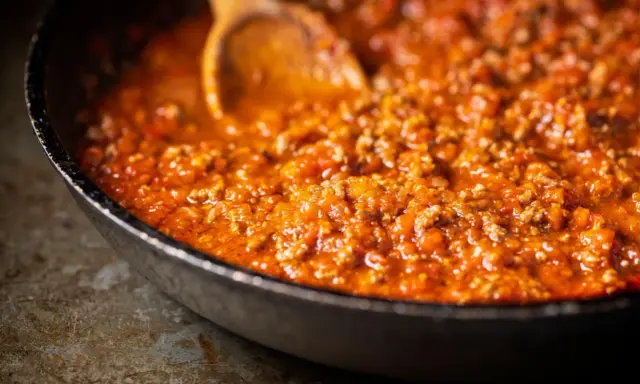 Eine Pfanne mit köstlicher, original italienischer Bolognese-Sauce, die mit einem Holzlöffel umgerührt wird.