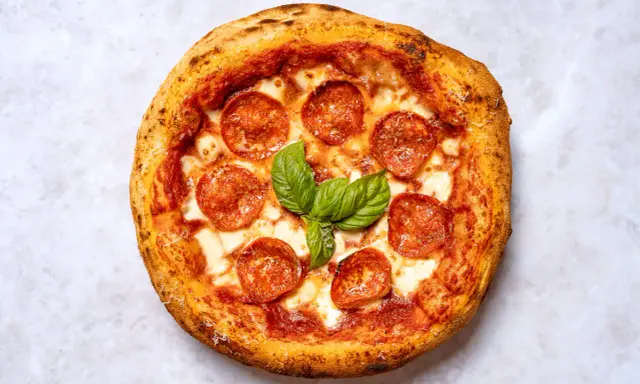 Eine köstliche New York Style Pizza mit Salami und frischem Basilikum, bereit zum Genießen.