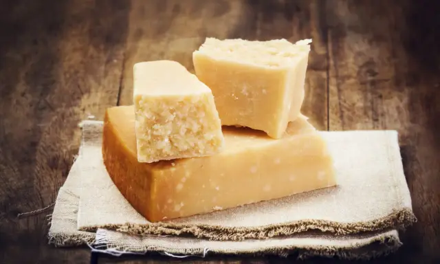 Drei Stücke Hartkäse, vielleicht Pecorino oder Parmesan, liegen auf einem Leinentuch vor rustikalem Holz.