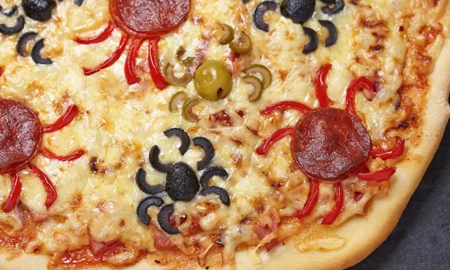 Gruselige Halloween-Pizza mit Spinnen aus Oliven und Salami, die über geschmolzenen Käse krabbeln.