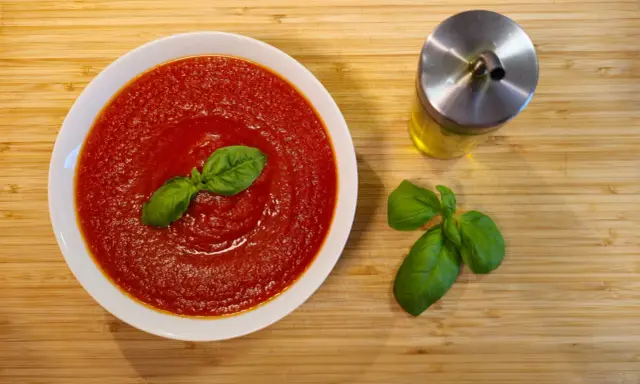 Schüssel mit cremiger Tomatensauce, garniert mit Basilikum. Daneben ein Glas Olivenöl und frische Basilikumblätter. Perfekt für Pasta mit San Marzano Tomaten.