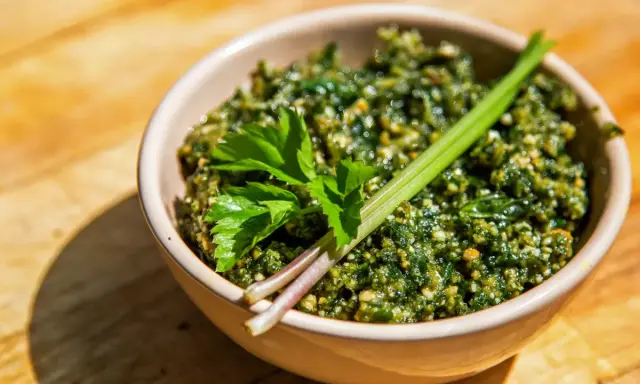 Schüssel mit würzigem Giersch Pesto, garniert mit frischen Kräutern auf Holzhintergrund.