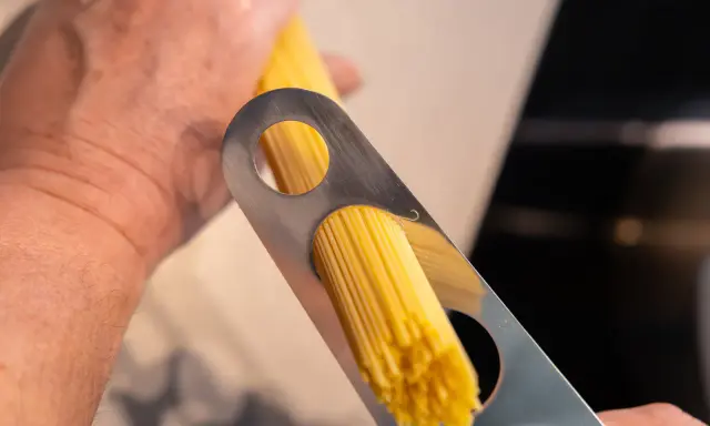 Ein Mann misst mit einem Metallwerkzeug die richtige Menge Spaghetti pro Person ab.