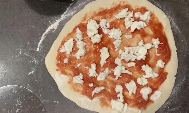 Ein roher Pizzaboden mit Tomatensauce und Mozzarella. Der pizzateig zieht sich zusammen, bereit für den Ofen.