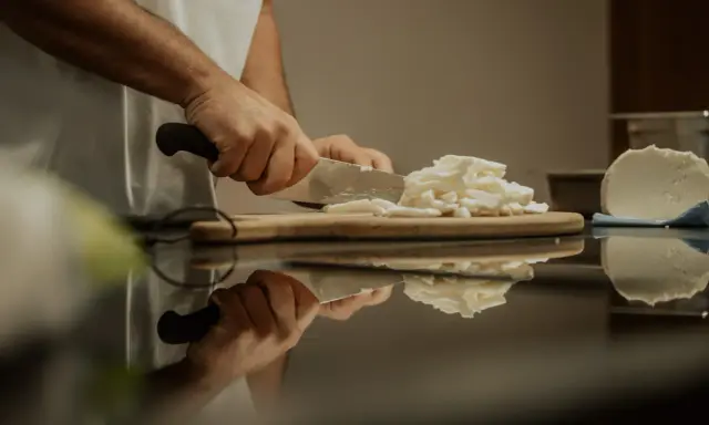 Hände schneiden Fior di Latte auf einem Holzbrett. Die frische Mozzarella-Masse wird für das Einfrieren vorbereitet.
