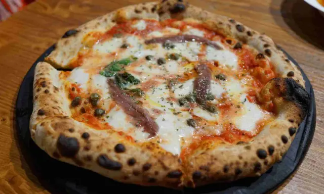 Eine original Pizza mit geschmolzenem Käse, Sardellen, Kapern und Basilikum.