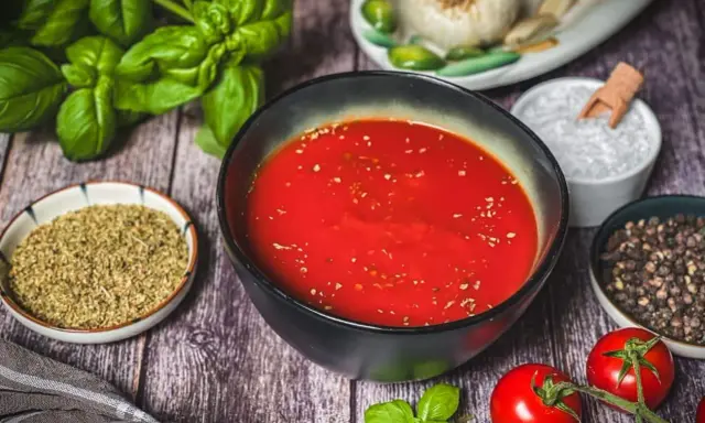 Schüssel mit original italienischer pizzasauce, umgeben von frischem Basilikum, Tomaten, Knoblauch, Salz und Pfeffer.