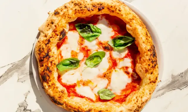 Eine klassische Pizza Napoli mit Tomaten, Mozzarella und frischem Basilikum. Der Belag ist einfach, aber perfekt für diese neapolitanische Spezialität.