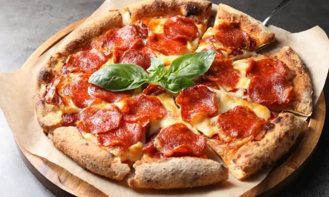 Eine köstliche Pizza mit geschmolzenem Käse und vielen Scheiben italienischer Salami, garniert mit frischem Basilikum.