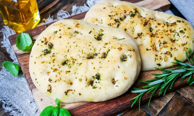 Zwei fluffige Pizzabrote mit Kräutern, perfekt gebacken mit Trockenhefe. Daneben frisches Basilikum und Rosmarin.
