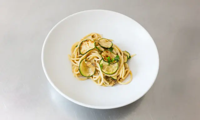 Spaghetti alla Nerano, ein cremiges Pastagericht mit gebratenen Zucchinischeiben, garniert mit frischen Kräutern, serviert auf einem weißen Teller.