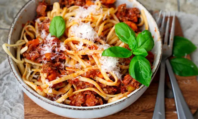 Eine Schüssel mit Linguine und einer herzhaften, **schnellen Bolognese**. Garniert mit frischem Basilikum und Parmesan.