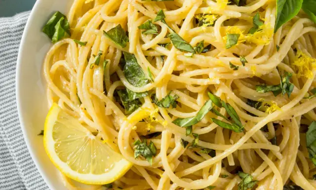 Spaghetti al limone, garniert mit frischem Basilikum und Zitronenschale, serviert mit einer Zitronenspalte.