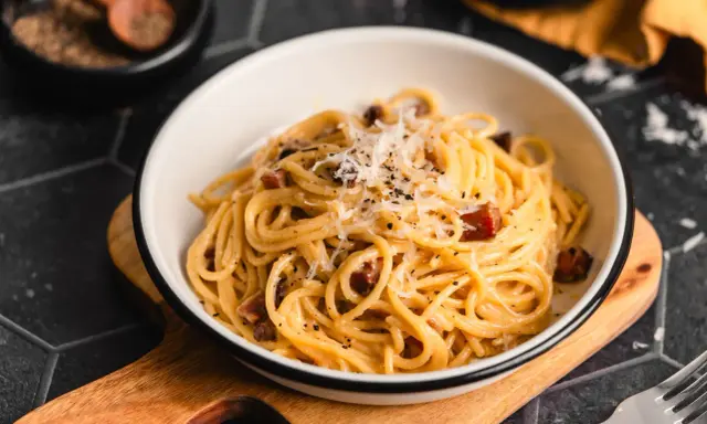 Eine Schüssel cremiger Spaghetti Carbonara, bestreut mit Parmesan und schwarzem Pfeffer, bereit zum Genießen.