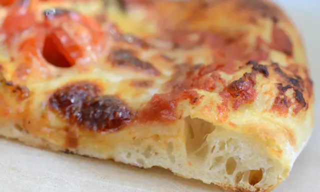 Ein Stück Pizza mit luftigem pizzateig, frisch aus dem pizzaofen. Der Teig ist goldbraun gebacken, die Tomatensoße und der Käse sind perfekt geschmolzen.